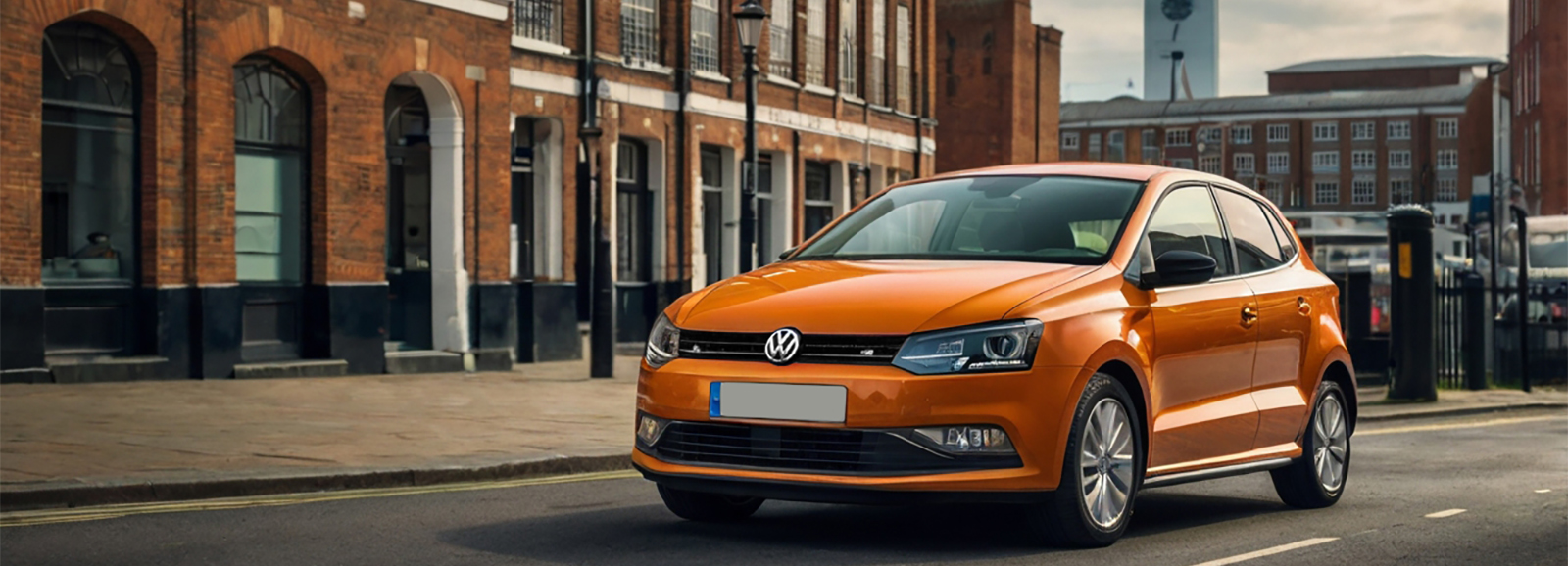 An Orange Volkswagen Polo Supermini car driving down a city street